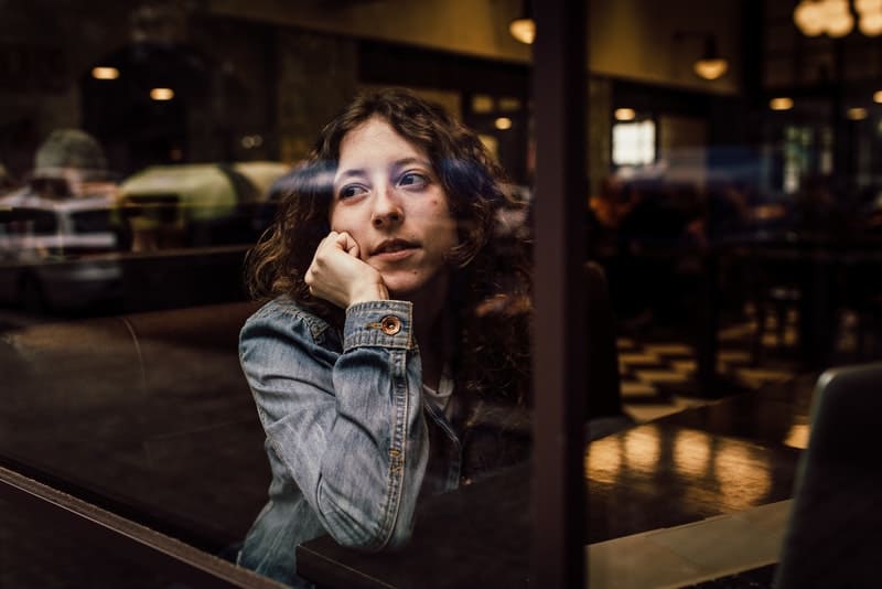 Eine Frau in Jeansjacke sitzt alleine in einem Café am Fenster