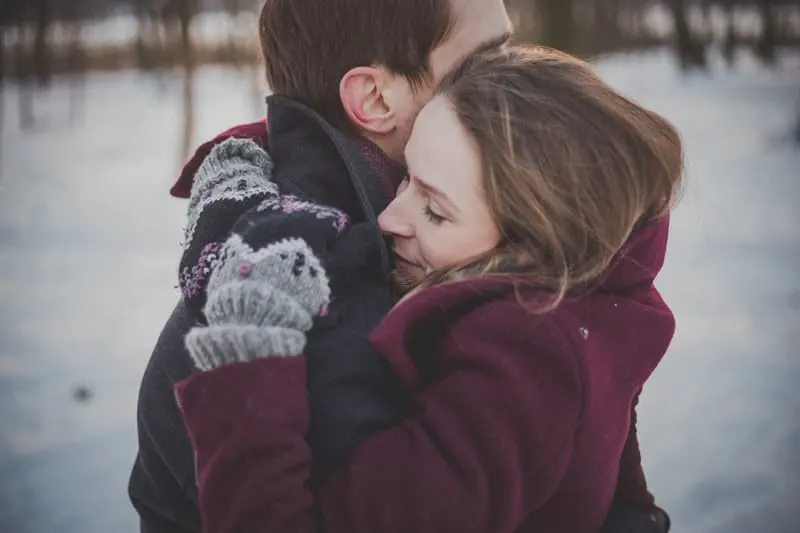 Eine Frau in Wollhandschuhen steht im Schnee und umarmt ihren Mann