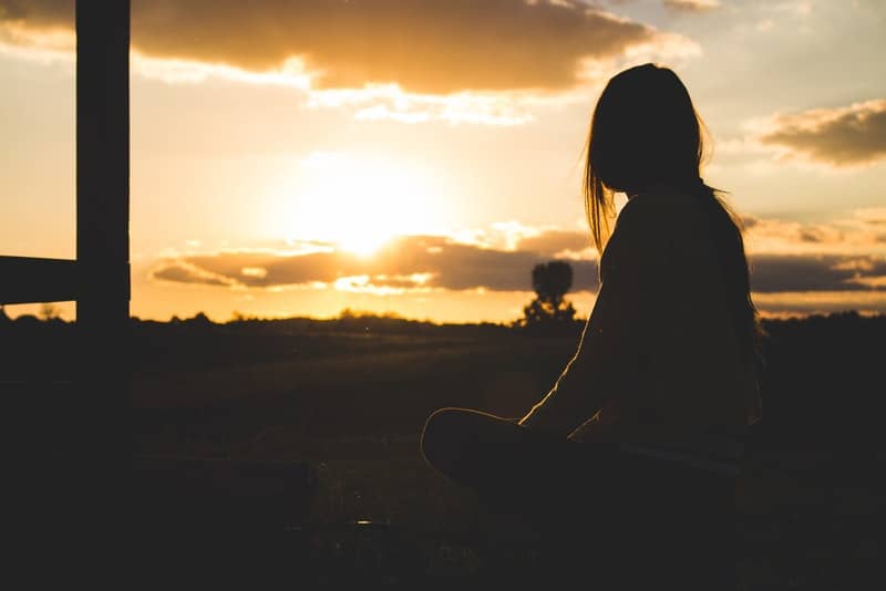 Eine Frau sitzt im Gras und beobachtet den Sonnenuntergang