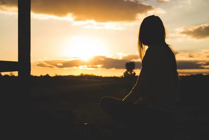 Eine Frau sitzt im Gras und beobachtet den Sonnenuntergang