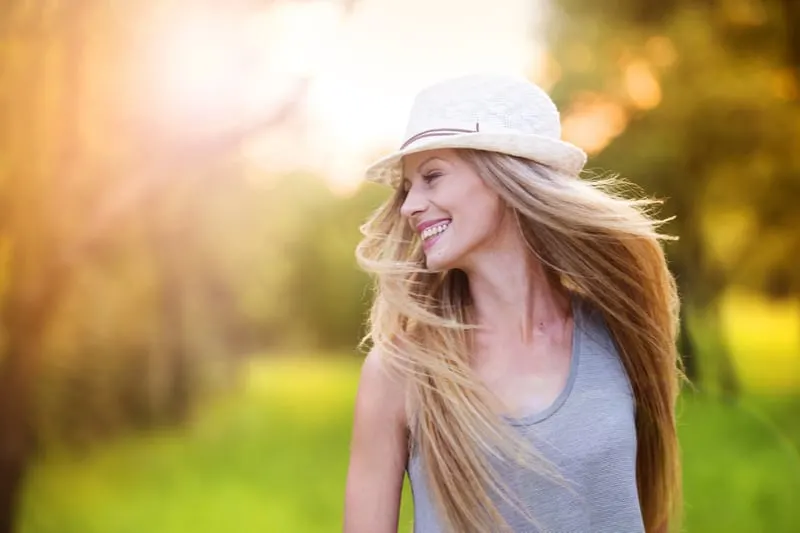 Eine glückliche Blondine mit weißem Hut genießt einen Spaziergang an einem sonnigen Tag