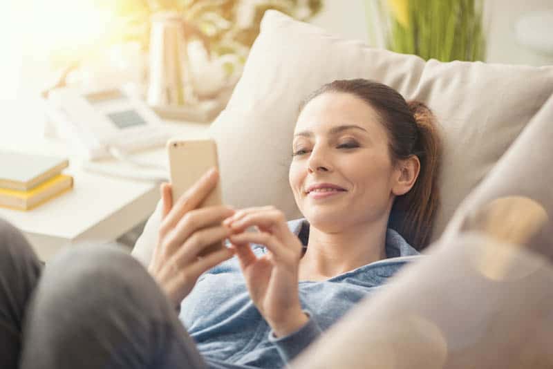 Eine lächelnde Frau liegt und flirtet über ihr Handy