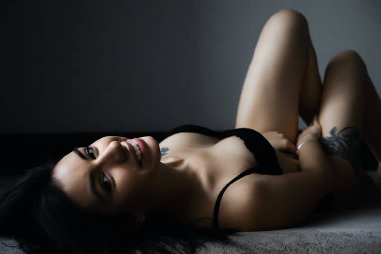 Mädchen in schwarzen sexy Dessous liegt auf dem Bett und lacht