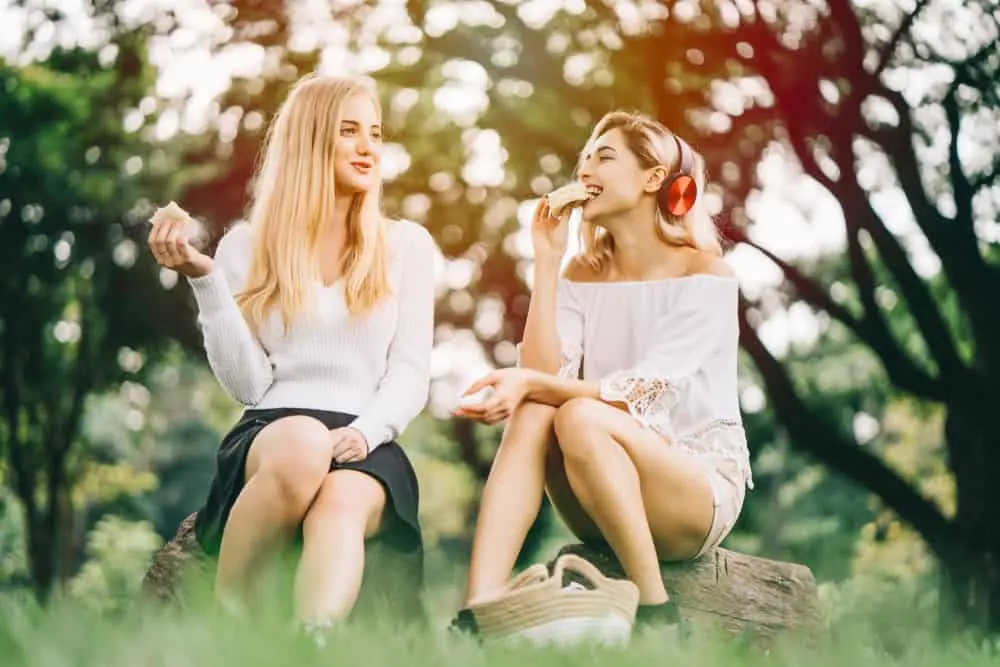 Zwei attraktive Blondinen sitzen im Park und essen und reden