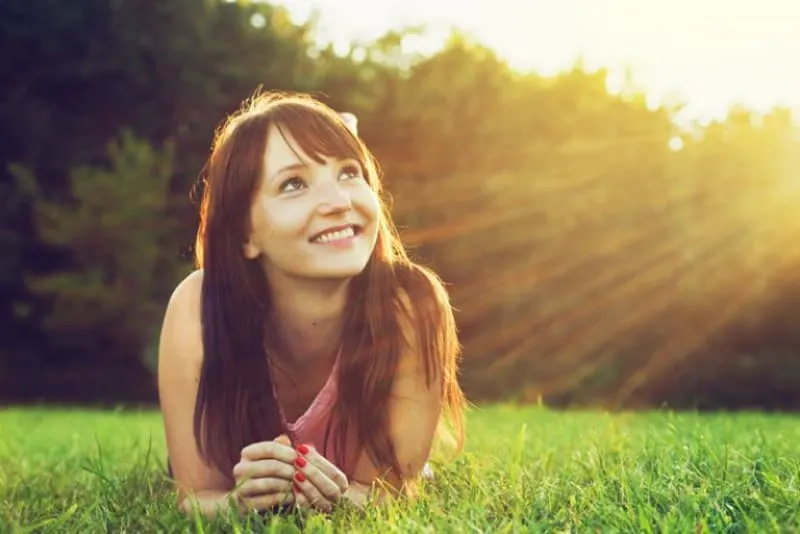 ein schönes junges Mädchen, das einen sonnigen Tag genießt, während sie im Gras liegt