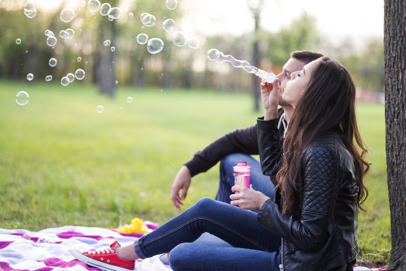 eine Frau, die mit ihrem Mann im Gras im Park sitzt und Blasen bläst