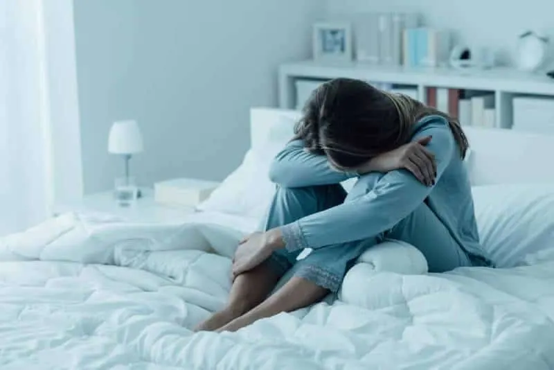 eine traurige Frau im blauen Pyjama, die auf dem Bett sitzt