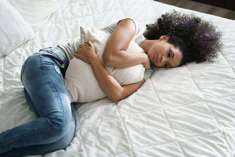 eine traurige afrikanische Frau, die auf dem Bett liegt und ein Kissen umarmt