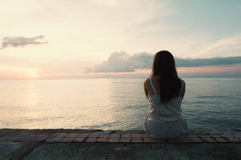 junge Frau, die allein hinten im Freien am Strand einer tropischen Insel sitzt