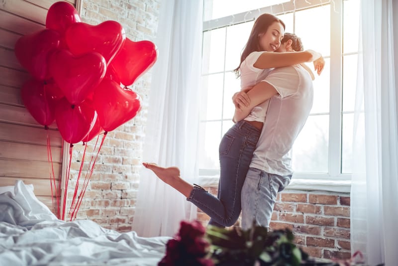 rote herzförmige Luftballons und ein liebevolles Paar in einer starken Umarmung