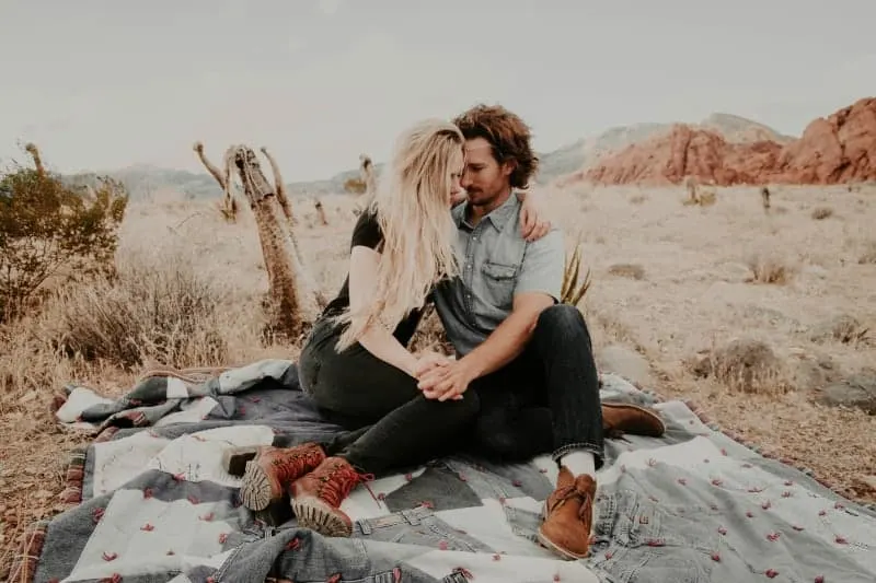 Auf dem Feld auf einer Decke sitzt ein liebevolles Paar in einer Umarmung Händchen haltend
