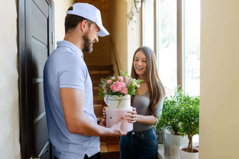 Der Lieferbote übergibt einem lächelnden Mädchen einen Geschenkstrauß