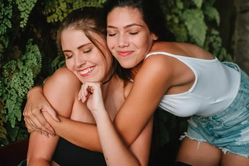 Die Brünette umarmt ihre Freundin hinter ihrem Rücken