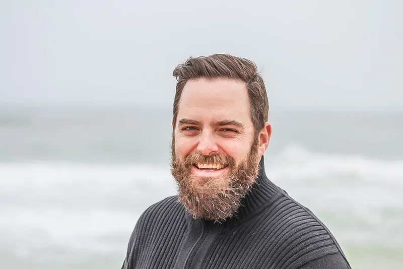 Ein lächelnder Mann mit Bart steht am Strand