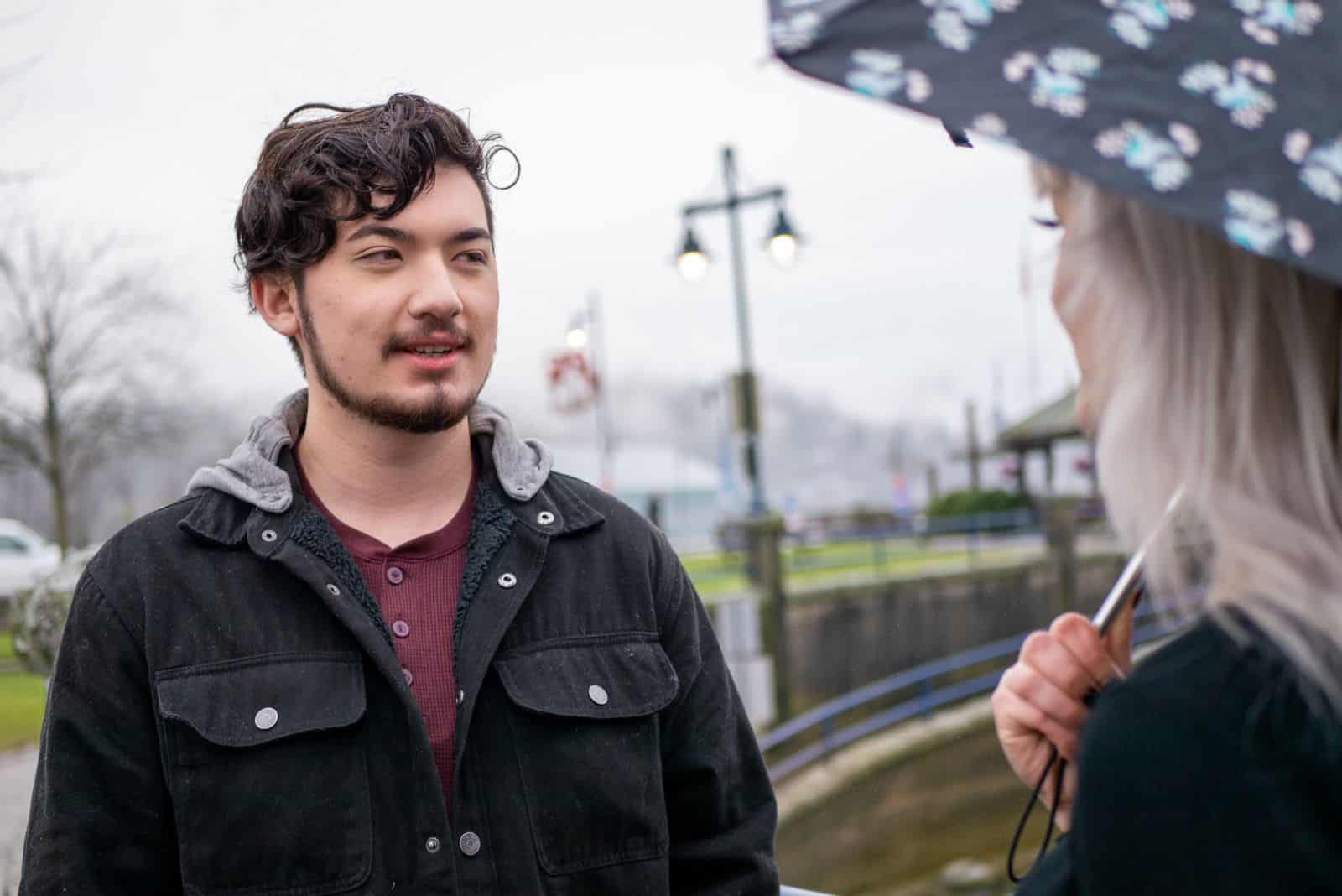 Ein Mädchen mit Regenschirm steht neben einem Mann und sie unterhalten sich