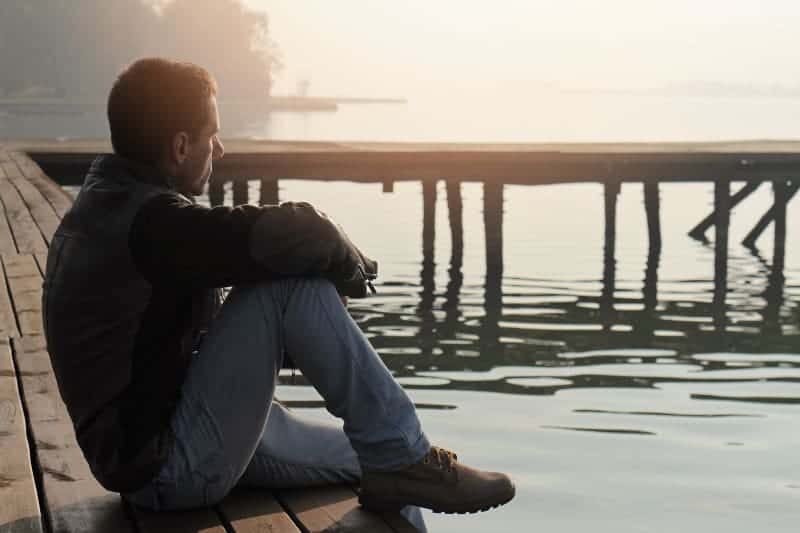 Ein Mann in Jacke und Jeans sitzt auf dem Pier am See