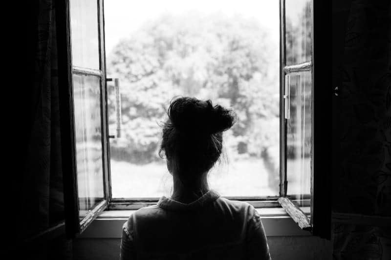 Eine Frau mit zusammengebundenen Haaren schaut aus dem Fenster