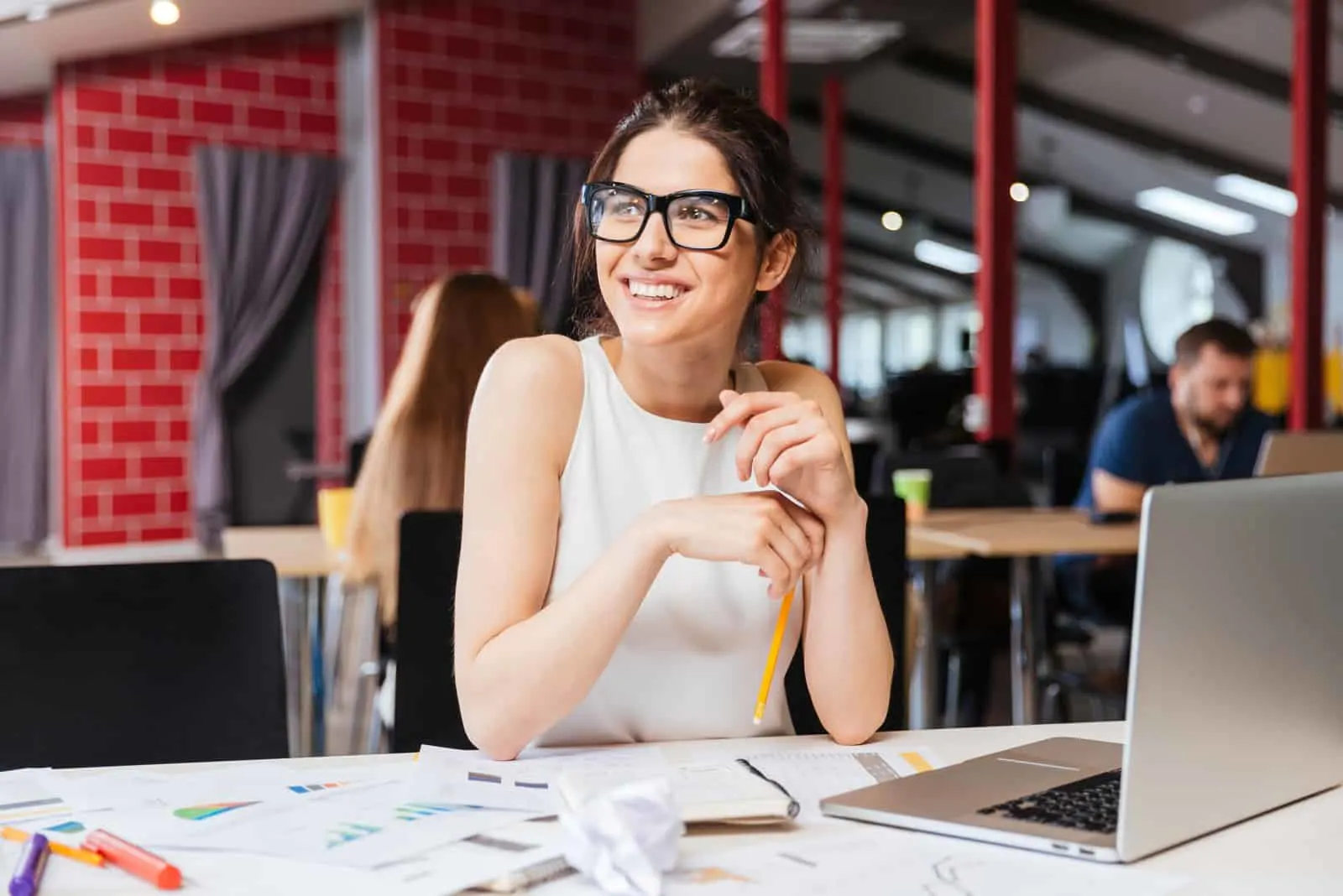 Eine lächelnde Geschäftsfrau mit Brille sitzt an ihrem Schreibtisch