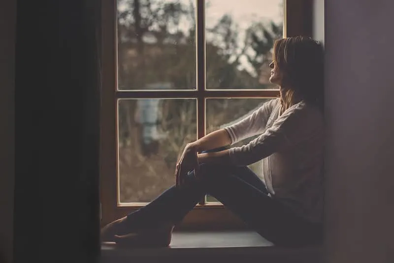traurige junge Frau, die am Fenster sitzt