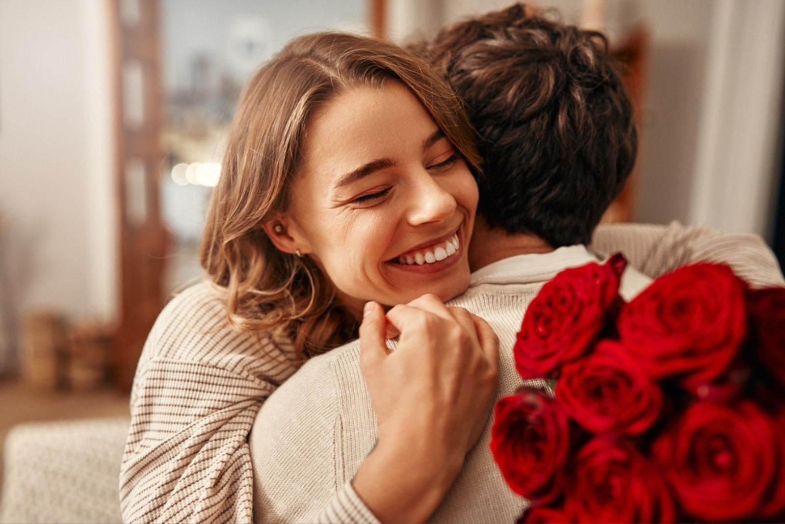 glueckliche Frau umarmt Mann mit Rosen