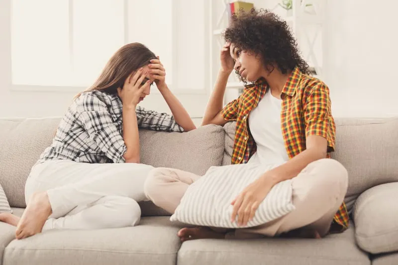 Zwei junge Studentinnen sitzen auf der Couch und besprechen Probleme