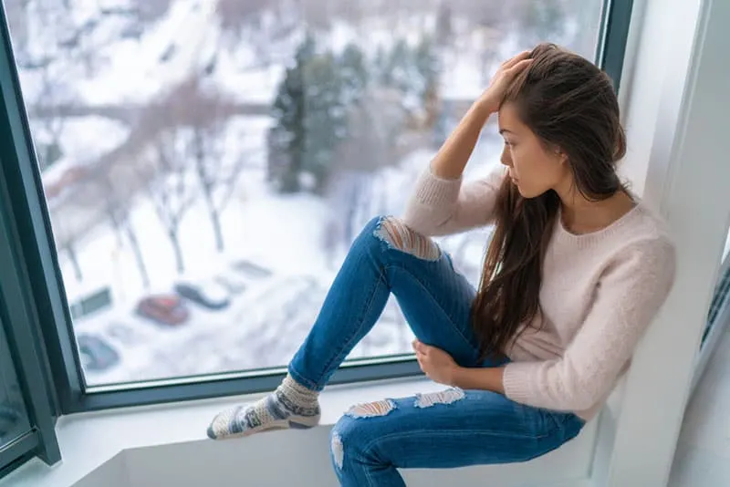 traurige junge Frau, die am Fenster sitzt und denkt