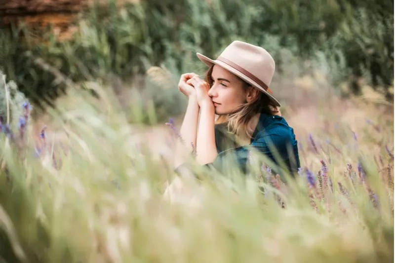 Eine schöne junge Dame mit Hut sitzt im Gras