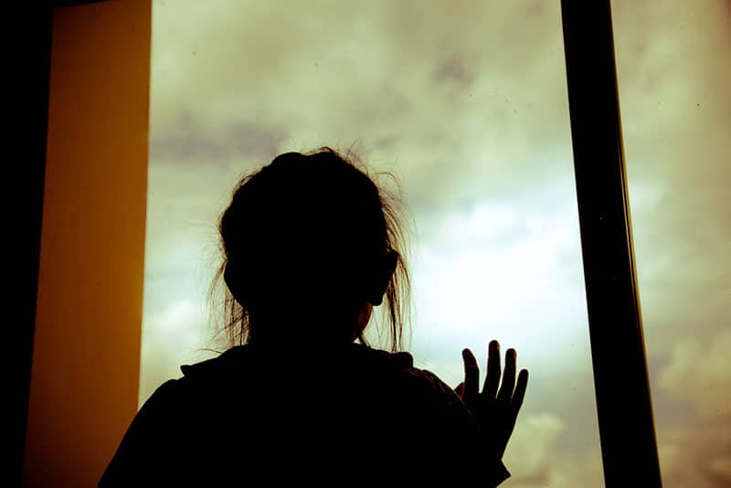 Silhouette der Frau, die Fenster zu Hause hält