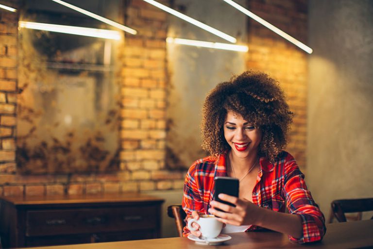 Afro-Frau, die Telefon ansieht und lächelt