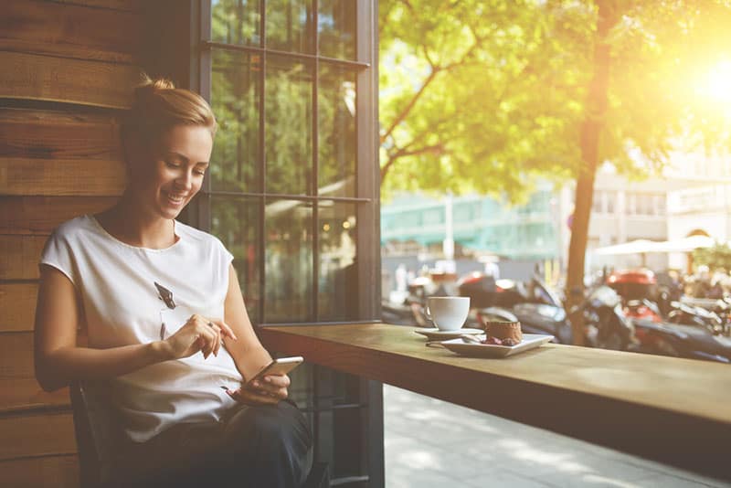 glückliche Frau, die am Telefon im Café tippt