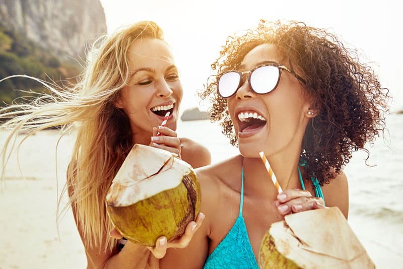 glückliche Frauen, die Kokosnuss am Strand trinken
