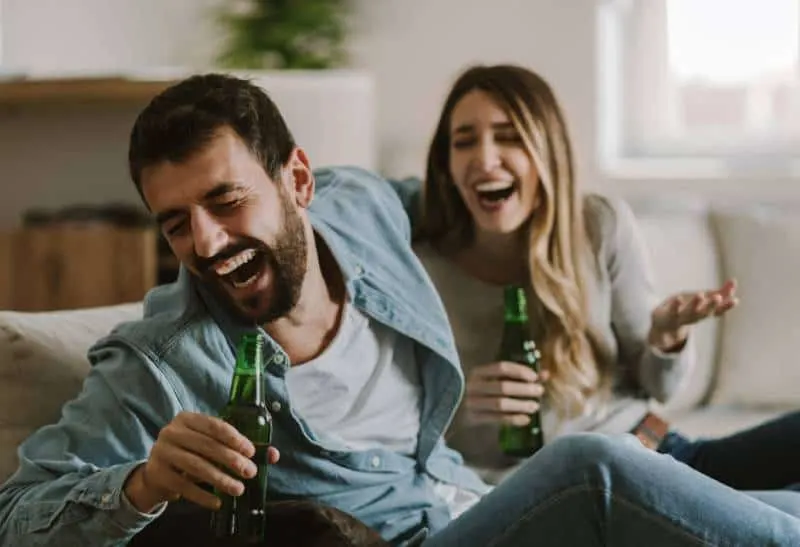 lachendes Paar sitzt im Wohnzimmer und trinkt Bier