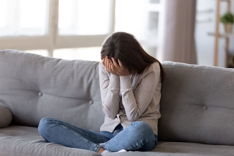 traurige Frau sitzt auf dem Bett und hält ihren Kopf