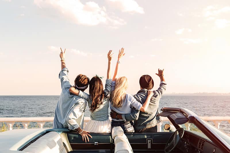 vier Freunde sitzen auf dem Auto vor dem Meer