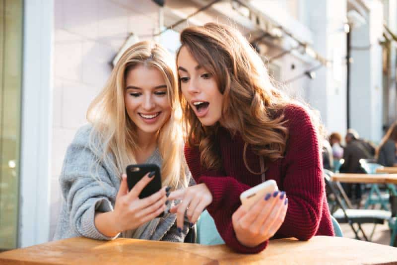 zwei Freundinnen, die sich im Café das Telefon anschauen