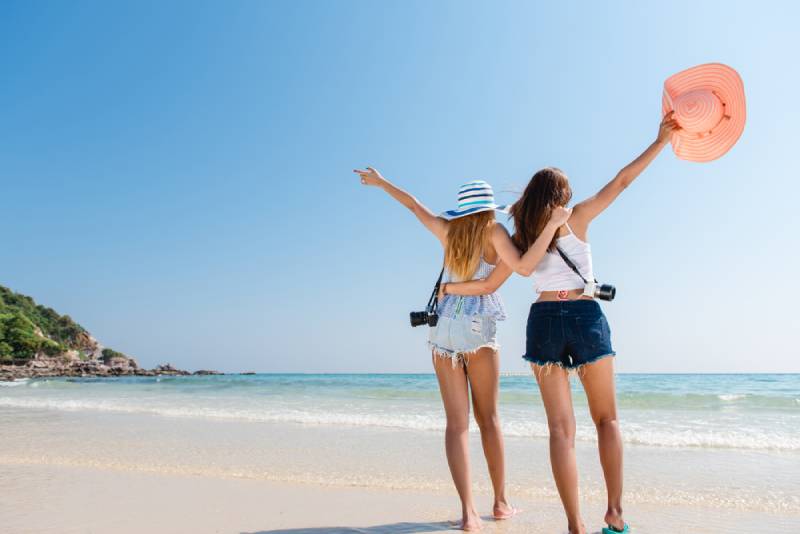zwei glückliche Freundinnen heben die Hand am Strand