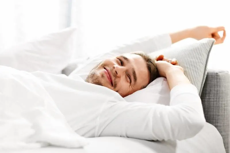 Bild zeigt jungen Mann, der sich im Bett ausdehnt