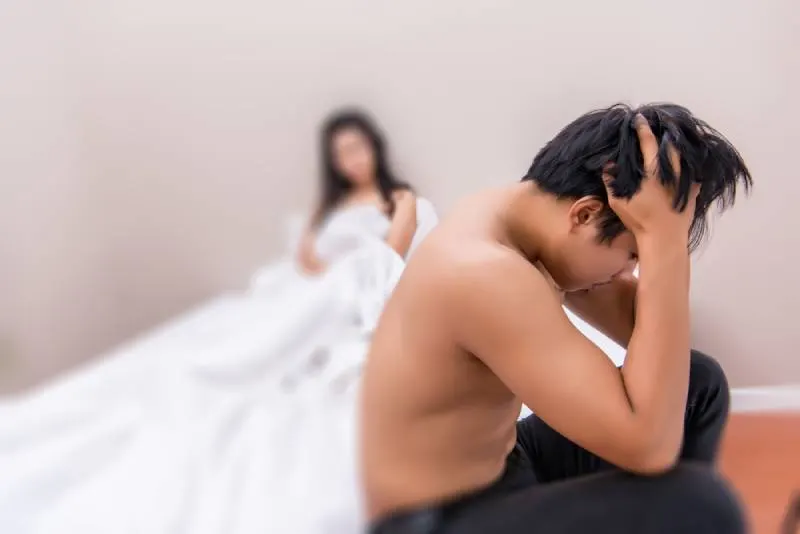Deprimierter junger Mann, der auf dem Bett sitzt und Probleme mit seiner Freundin im Zimmer hat