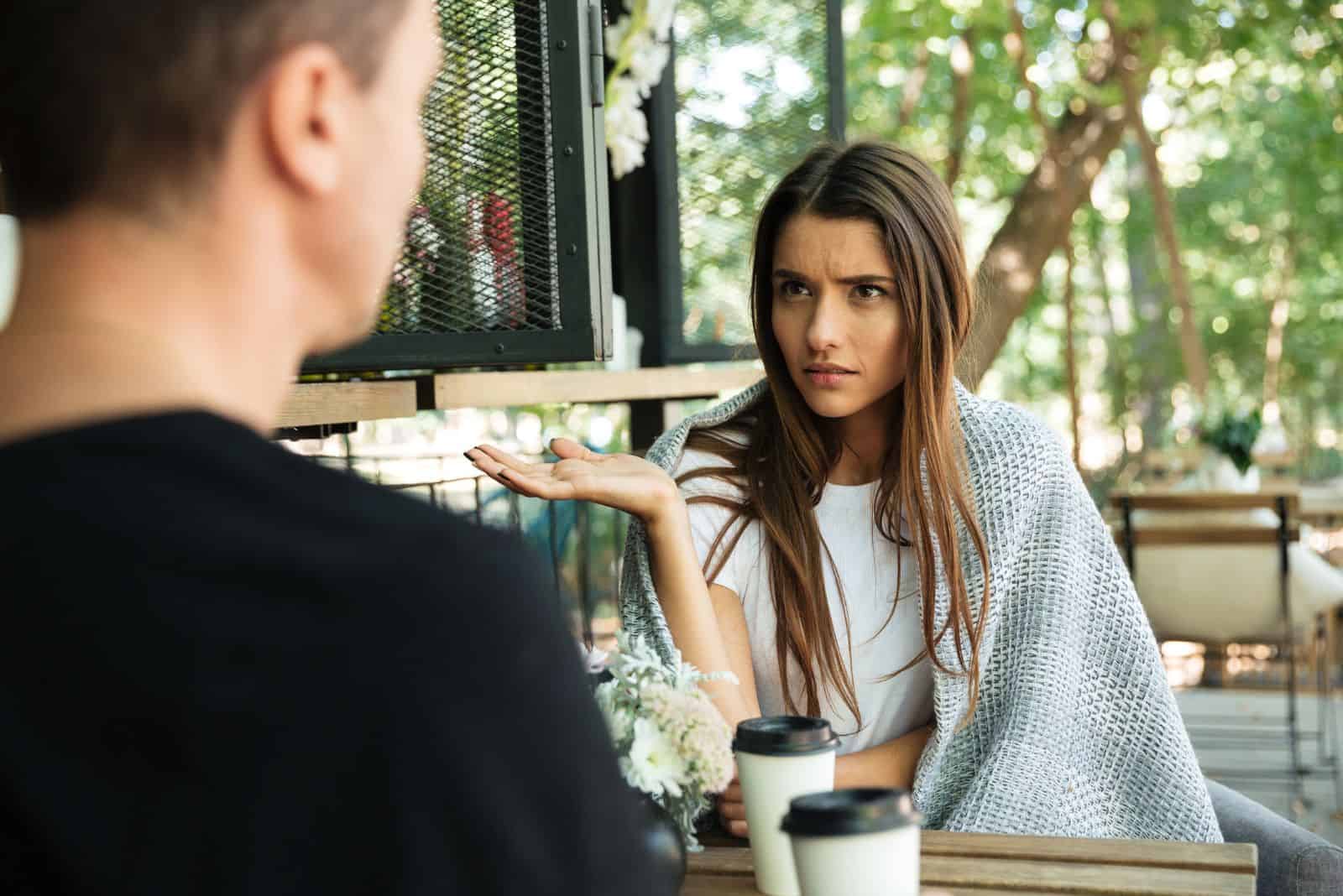 Eine Frau mit langen braunen Haaren spricht verwirrt mit einem Mann
