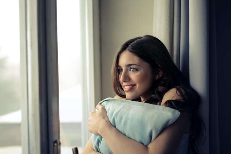 Eine schöne Frau umarmte ein Kissen am Fenster