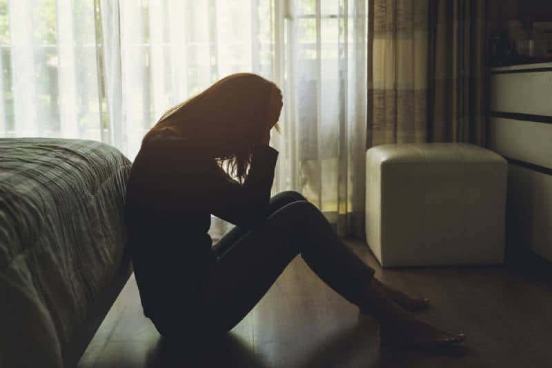 Einsame junge Frau depressiv und gestresst sitzend Kopf in Händen im dunklen Schlafzimmer,