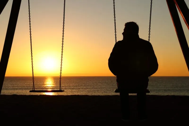 ein Mann sitzt auf der Schaukel bei Sonnenuntergang