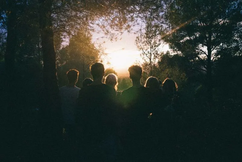 mehrere Leute beobachten den Sonnenaufgang mitten im Wald