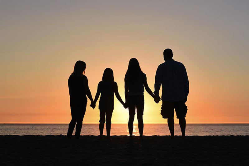 Familie, die ihre Hände im Sonnenuntergang zusammenhält