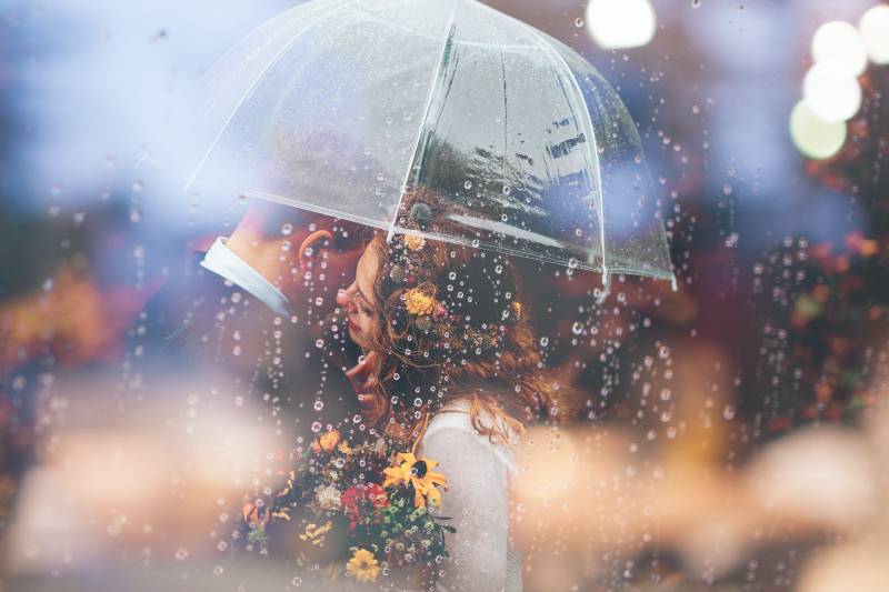 Frau, die Mann unter Regenschirm während des Regens umarmt