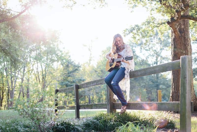 Frau, die auf Zaun sitzt, während sie Gitarre spielt