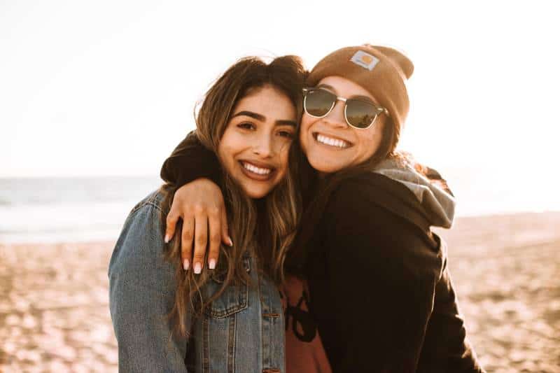 Frau, die eine andere Frau umarmt, während sie am Strand lächelt