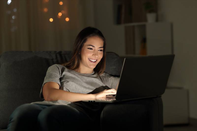 Frau, die einen Laptop in der Nacht sitzt auf einer Couch im Wohnzimmer zu Hause sitzt