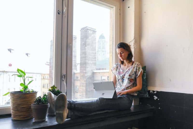 Frau, die weißes und rotes Blumenoberteil trägt, das neben Fenster sitzt