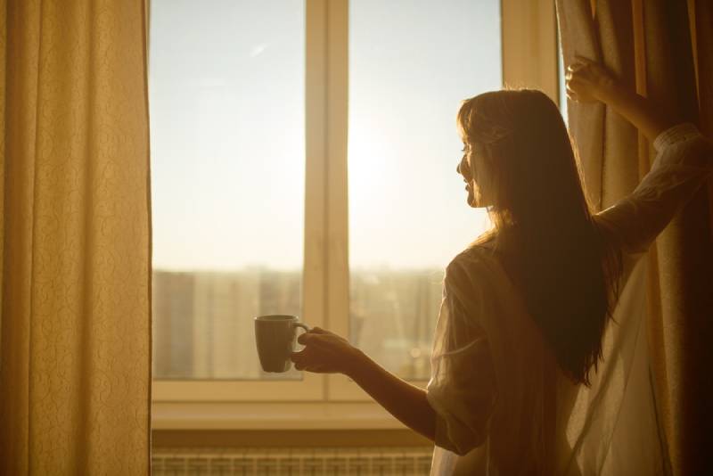 Frau hält eine Tasse mit heißem Tee und schaut auf den Sonnenaufgang